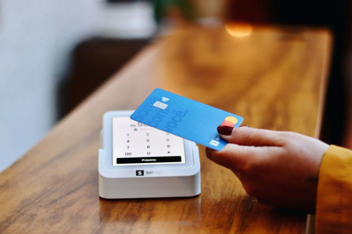 Person holding a blue credit card making a contactless payment on a card reader.