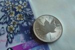 Close-up of a Canadian silver maple leaf coin resting on a colorful Canadian banknote.