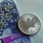 Close-up of a Canadian silver maple leaf coin resting on a colorful Canadian banknote.