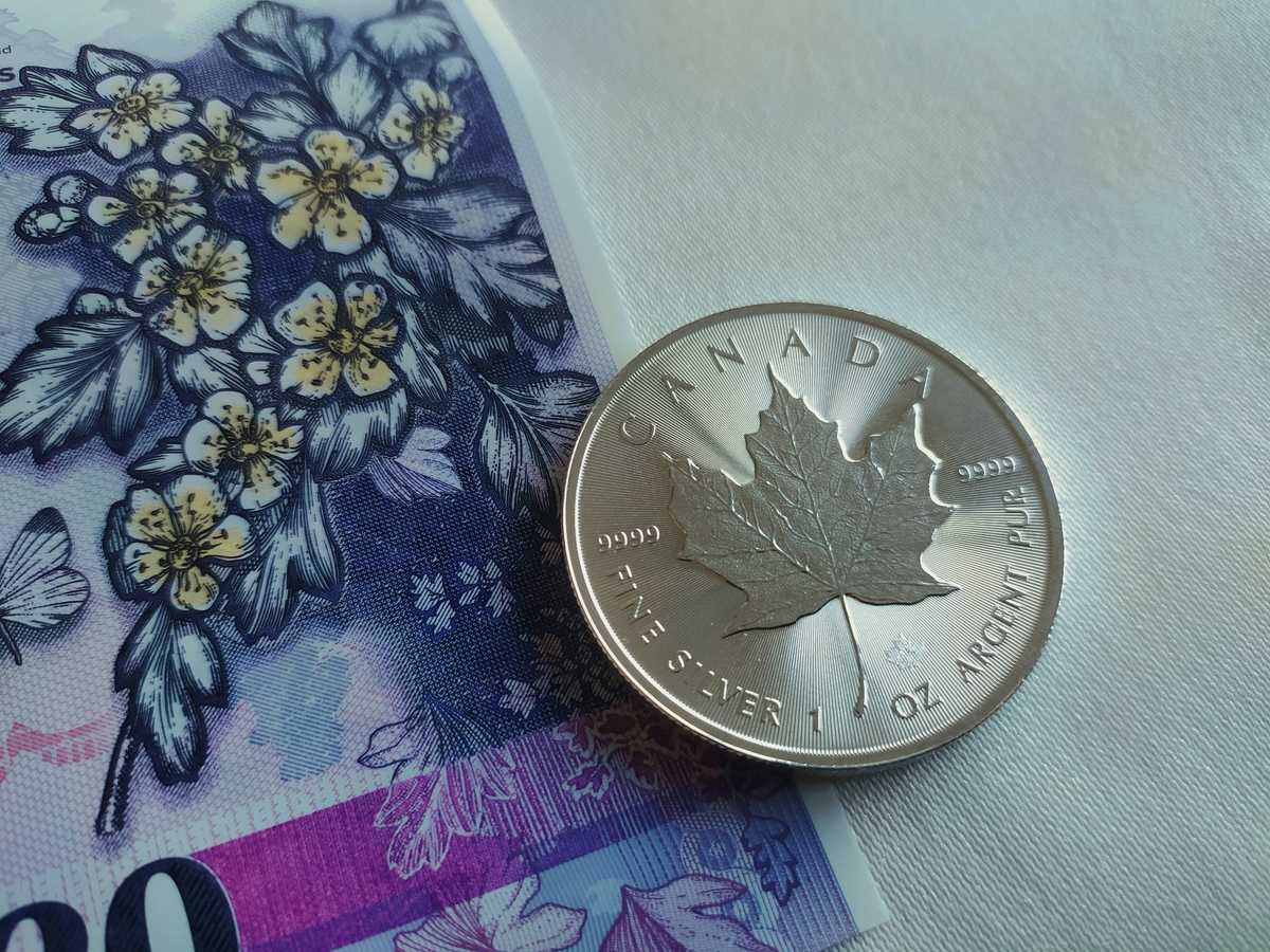 Close-up of a Canadian silver maple leaf coin resting on a colorful Canadian banknote.
