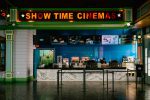 Modern movie theater concession counter with bright “Show Time Cinemas” sign above and a staff member preparing snacks.