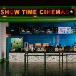 Modern movie theater concession counter with bright “Show Time Cinemas” sign above and a staff member preparing snacks.