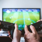 Two people holding game controllers while playing a football video game on TV.