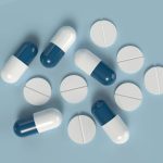 Blue and white capsules with round tablets on a light blue background representing modern pharmaceuticals.
