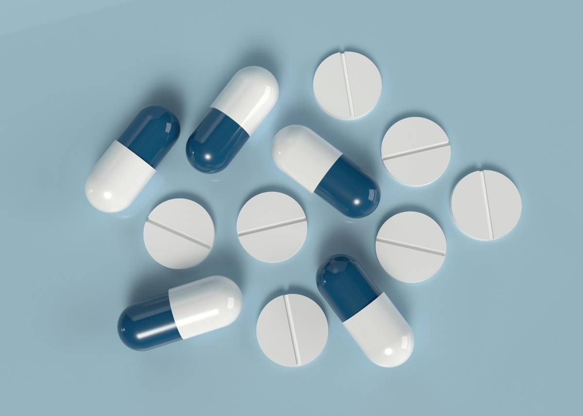 Blue and white capsules with round tablets on a light blue background representing modern pharmaceuticals.