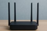 A modern Wi-Fi 7 router with four antennas placed on a light wooden desk against a soft blue-gray wall.