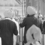 Two Sikh men wearing traditional blue attire and yellow turbans walk together among a crowd, symbolizing Punjab’s vibrant culture and unity.