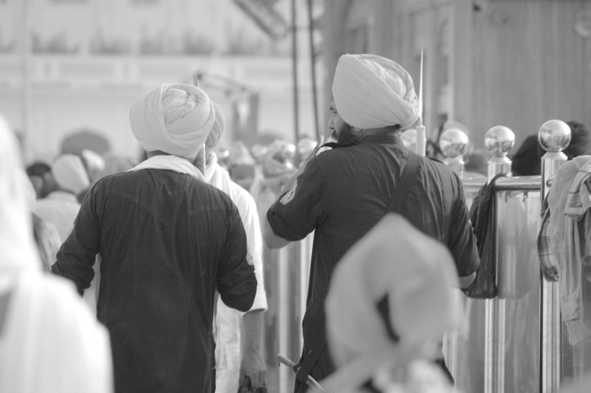 Two Sikh men wearing traditional blue attire and yellow turbans walk together among a crowd, symbolizing Punjab’s vibrant culture and unity.