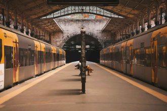 A quiet train station with two yellow commuter trains facing each other and passengers sitting on benches under the roofed platform.