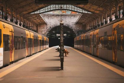 A quiet train station with two yellow commuter trains facing each other and passengers sitting on benches under the roofed platform.