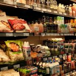 A grocery store aisle filled with colorful packaged foods, drinks, and dairy products neatly arranged on shelves under warm lighting.