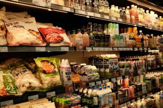 A grocery store aisle filled with colorful packaged foods, drinks, and dairy products neatly arranged on shelves under warm lighting.