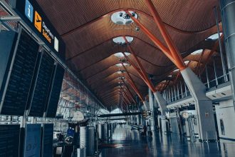 Modern airport departure hall with bright lighting, large display boards, and travelers walking through the spacious terminal.