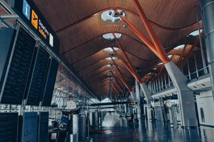 Modern airport departure hall with bright lighting, large display boards, and travelers walking through the spacious terminal.
