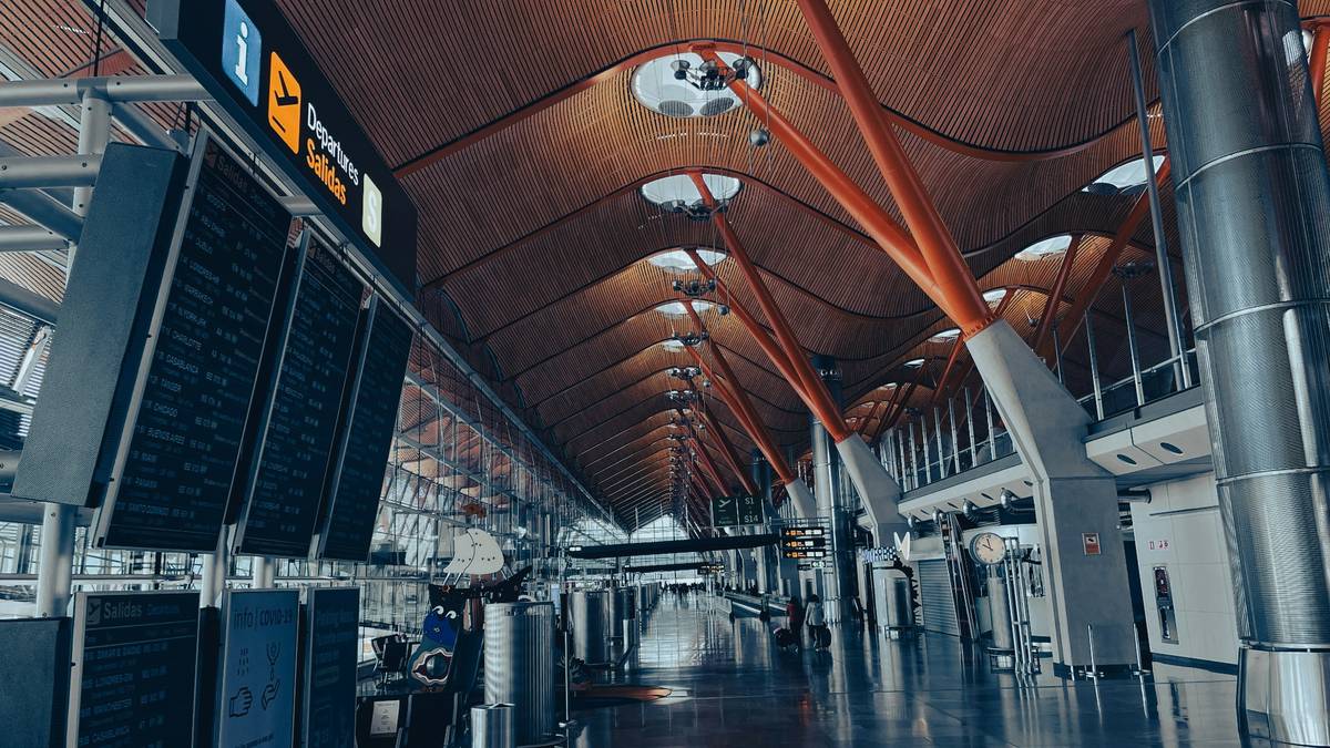 Modern airport departure hall with bright lighting, large display boards, and travelers walking through the spacious terminal.