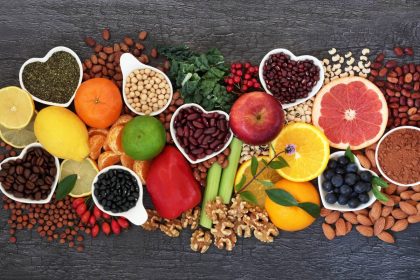 A colorful assortment of high-protein and high-fiber foods including beans, nuts, citrus fruits, and vegetables arranged on a dark wooden surface.
